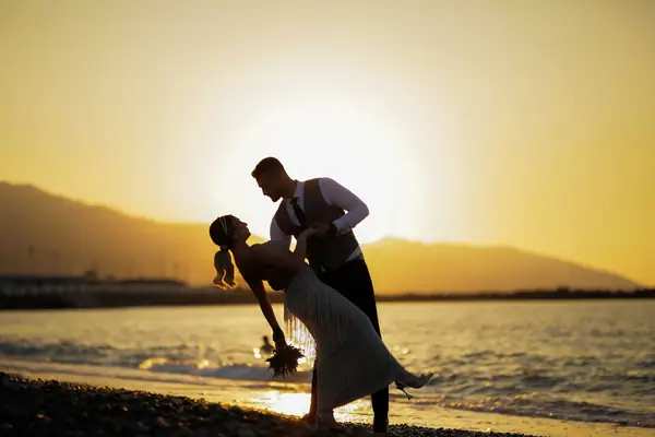 Groom dipping the bride on a beach at sunset