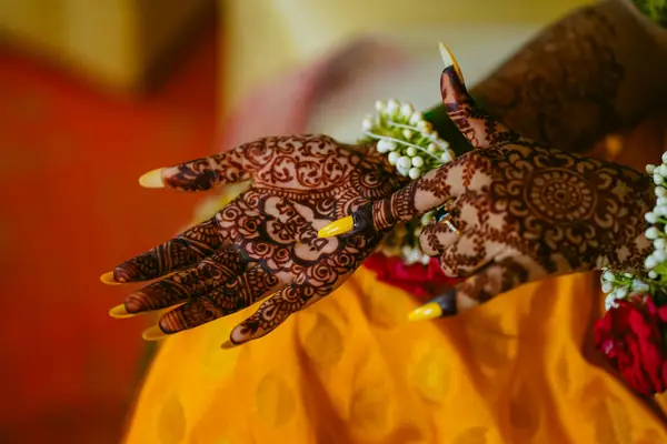 Mehendi hand holding flowers against a yellow lehenga